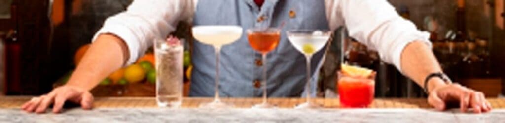 Ein Barkeeper steht hinter einer Bar mit verschiedenen Cocktails auf der Theke.