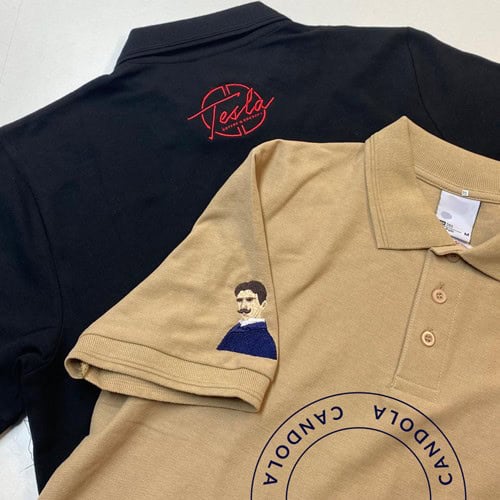 Das Bild zeigt zwei Hemden oder Poloshirts, eines mit einem Tesla-Logo und das andere mit einer Abbildung von Nikola Tesla und Schriftzügen.